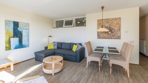 A modern living room with a sectional sofa, a round coffee table, and a dining area with a glass table and chairs. - Apartment 189 in Julianadorp aan Zee (Julianadorp)