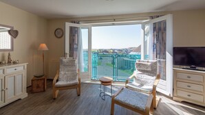 A room with two patterned chairs, a TV, a lamp, and a view of a balcony with a railing. - Apartment 189 in Julianadorp aan Zee (Julianadorp)