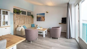 A modern living room with a wooden floor, a sofa, two armchairs, a coffee table, and a TV. - Apartment by the Dunes Near the Sea (Julianadorp)