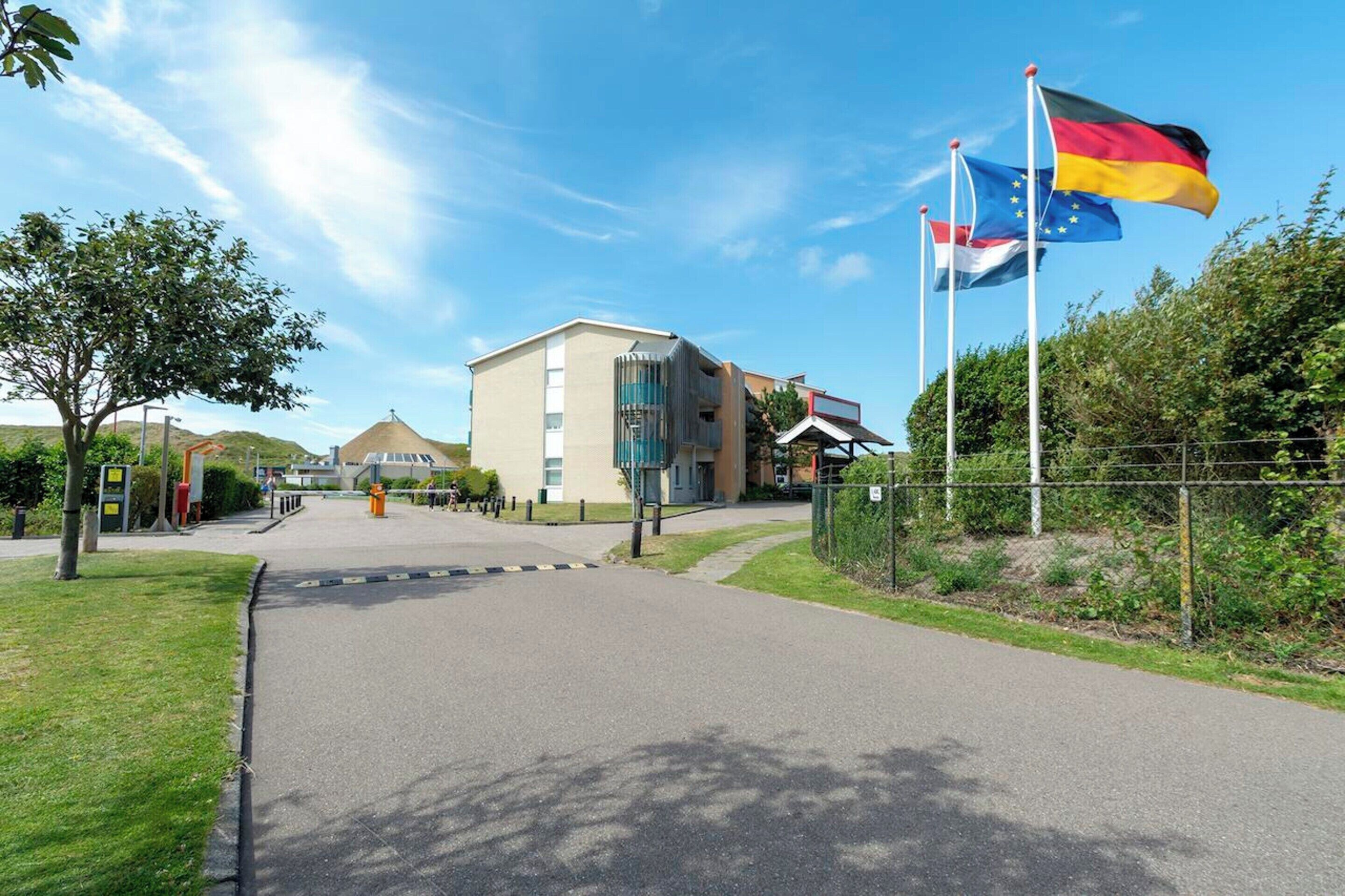 A building with a modern architectural style, a paved entrance, and flags on poles.