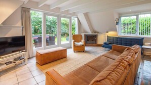 Uma sala de estar ampla, com uma televisão grande, assentos confortáveis, lareira e janelas grandes que oferecem vista para o exterior.