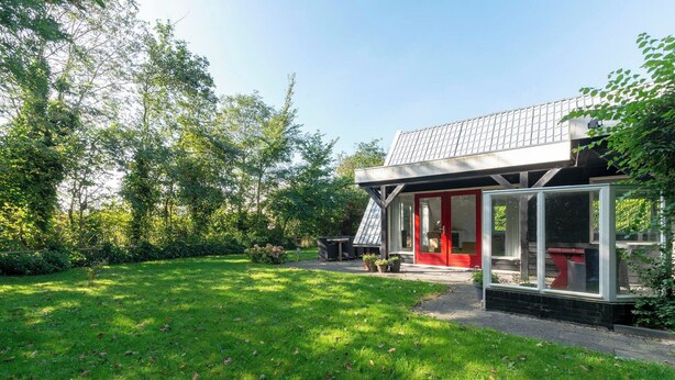 A modern house with a red door, large windows, and a garden.