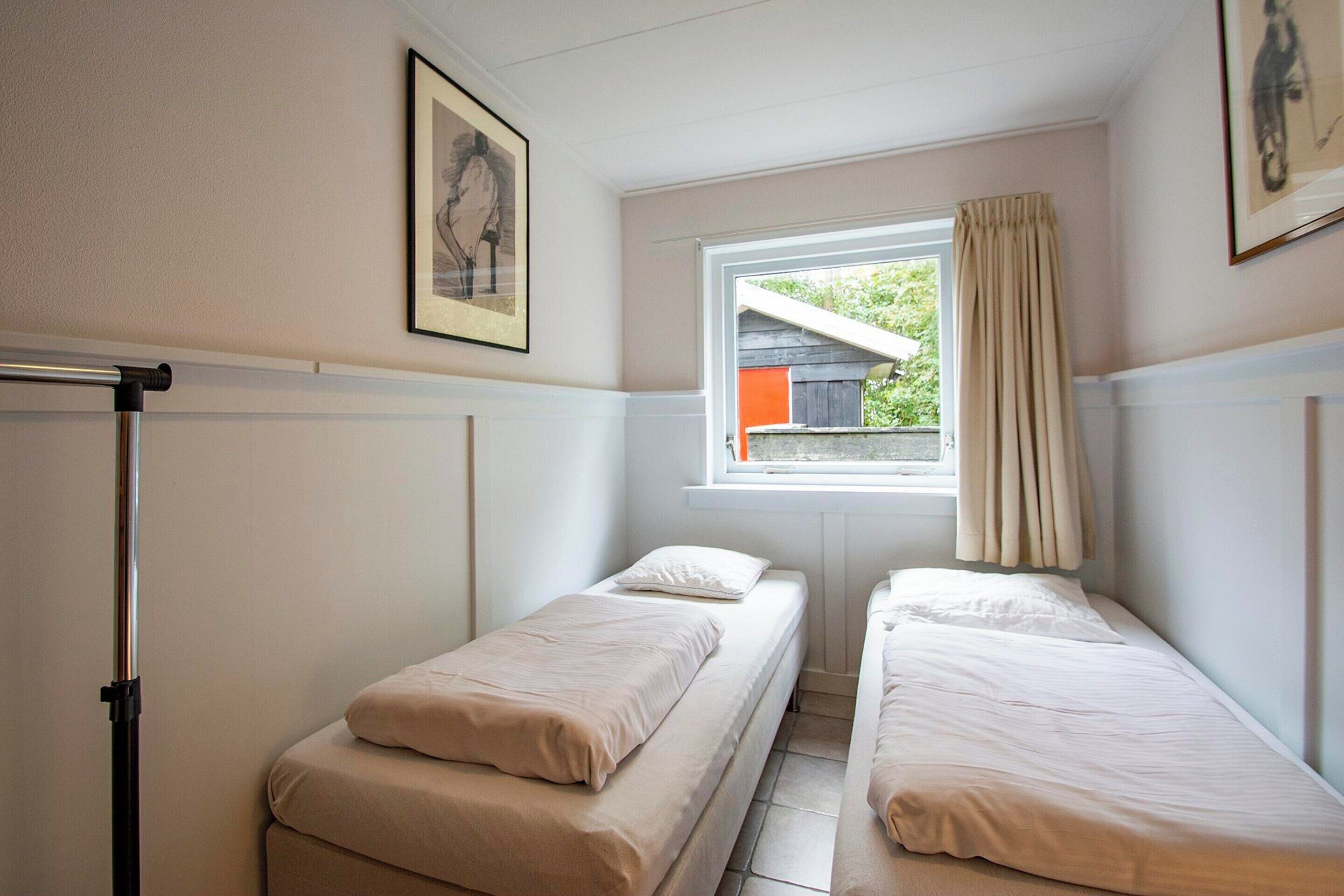 A small, clean room with two single beds, a window with curtains, and a radiator.