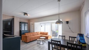 A modern living room with a sofa, a dining table, and a TV. - Holiday Home in Texel Near the Beach (De Koog)