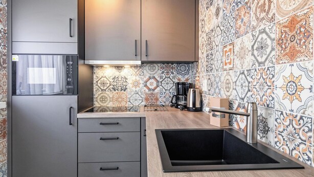 A modern kitchen with grey cabinets, a stainless steel refrigerator, a coffee maker, and a sink. - Holiday Home in Texel Near the Beach (De Koog)