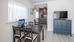 A modern kitchen with a dining area, a TV on a cabinet, and a bag of chips on the table. - Holiday Home in Texel Near the Beach (De Koog)