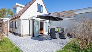 A modern house with a patio area featuring a table and chairs, a large umbrella, and a sliding glass door leading to an interior room. - Holiday Home in Texel Near the Beach (De Koog)