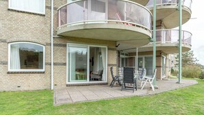 En boligbygning med facade i mursten, en balkon med glasværn, og en patio med udendørs møbler.