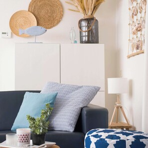 Een moderne woonkamer met een donkere bank, gestreepte kussens, een tafeltje met een plant, een lamp en decoratieve items op een wit kastje.