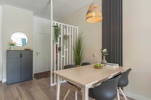 A modern dining area with a wooden table, black chairs, a hanging light fixture, and a white partition with plants.