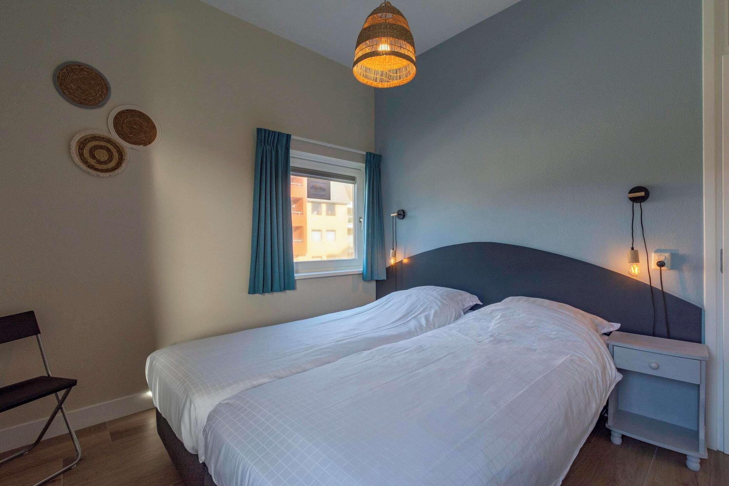Un dormitorio con dos camas, una ventana con cortinas, una lámpara colgante y una lámpara fijada a la pared.