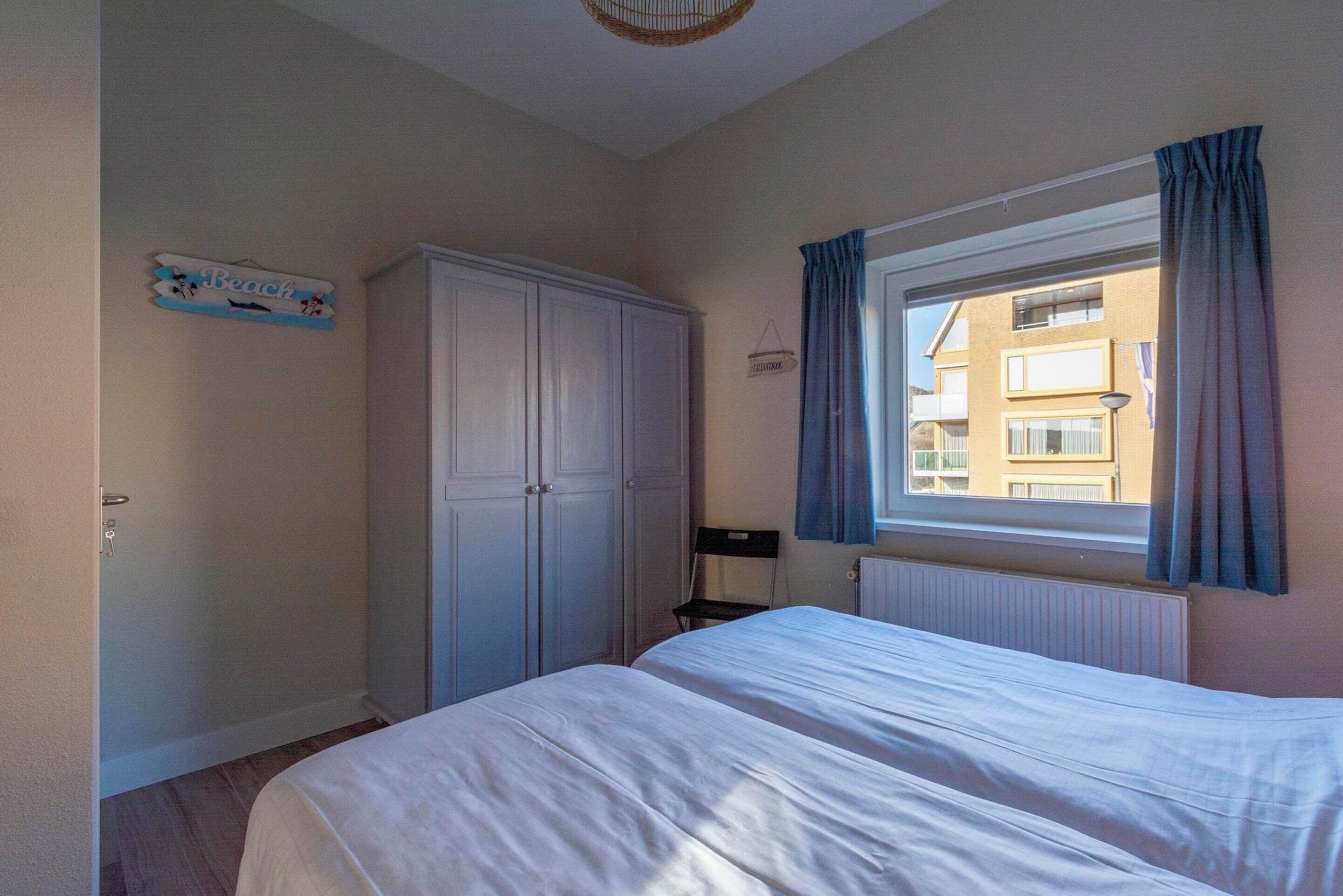 A bedroom with a bed, a wardrobe, a window with curtains, and a sign on the wall.