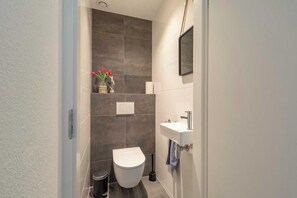 A modern bathroom with a toilet, sink, and a small shelf with a vase of flowers.