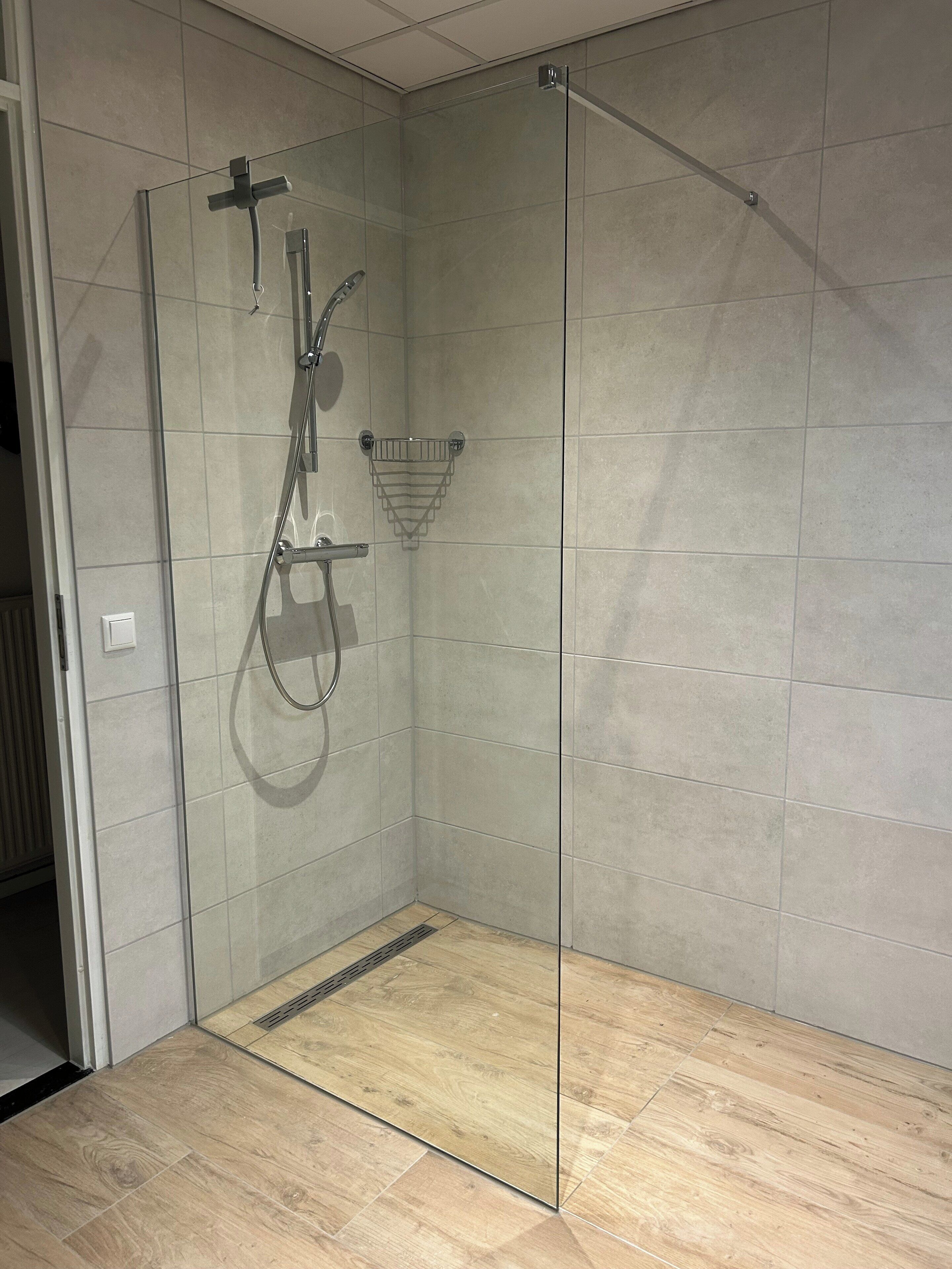 A glass-enclosed shower with a handheld showerhead and a wall-mounted faucet.
