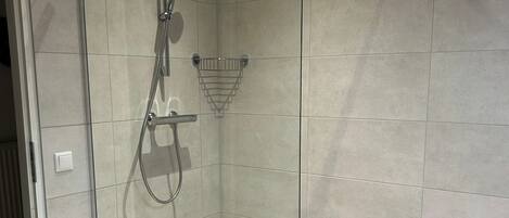 A glass-enclosed shower with a handheld showerhead and a wall-mounted faucet.