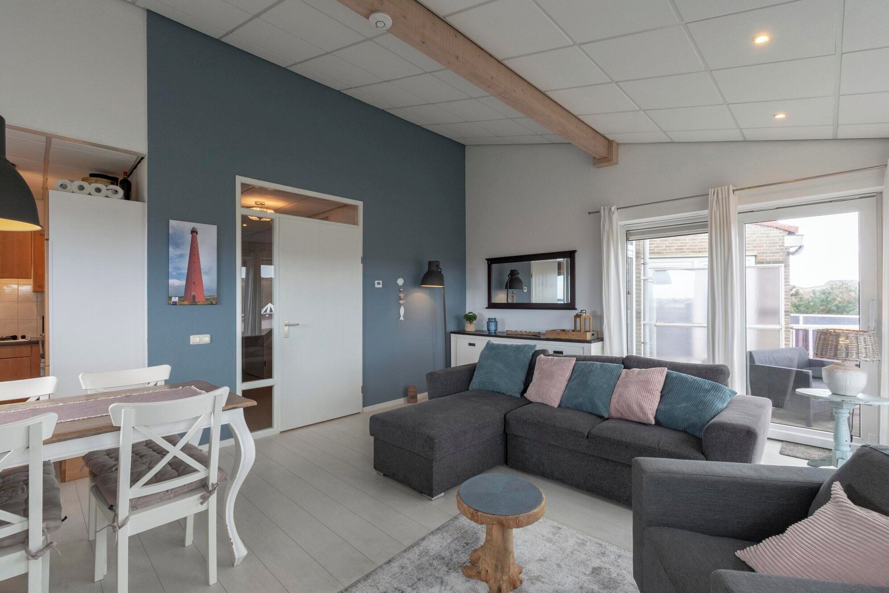 Ein modernes Wohnzimmer mit einer grauen Eckcouch, einem Holzespeisetisch mit weißen Stühlen und einem kleinen runden Couchtisch.