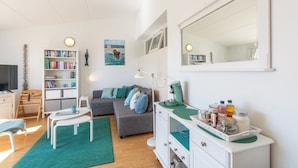 A modern living room with a grey sofa, a white cabinet with jars, a bookshelf, and a large mirror. - Apartment in Julianadorp by the Sea (Julianadorp)