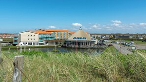 A waterfront hotel with a central round building, a modern building with orange roofs, and a river in the foreground. - Apartment in Julianadorp by the Sea (Julianadorp)