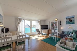 A bright living room with a dining area, a sofa, a bookshelf, and a television.
