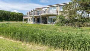 A two-story house with a balcony, a grassy yard, and a forested hill in the background. - Modern Home Near the Beach (Julianadorp)