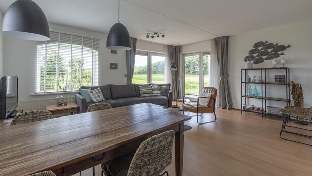 A modern living room with a wooden dining table, two sofas, a TV, and a bookshelf. - Modern Home Near the Beach (Julianadorp)