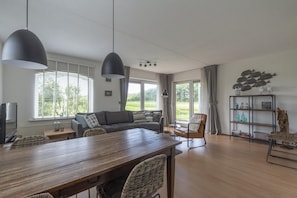A modern living room with a wooden dining table, two sofas, a TV, and a bookshelf. - Modern Home Near the Beach (Julianadorp)