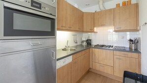 A modern kitchen with stainless steel appliances, wooden cabinets, and a black countertop. - Modern Home Near the Beach (Julianadorp)