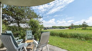A covered outdoor seating area with white chairs and a small table, overlooking a parking lot and a grassy field. - Modern Home Near the Beach (Julianadorp)