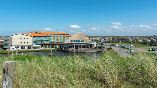 A waterfront hotel with a central building featuring a circular structure with a conical roof, surrounded by a water body and a parking area. - Apartment by Dutch Beach Pet-friendly (Julianadorp)