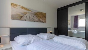 Una camera d'albergo con un letto grande, una testiera, un comodino e un quadro appeso al muro, oltre a uno specchio.