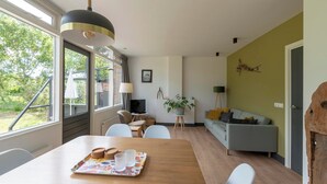A modern living room with a dining table, sofa, and a large window offering a view of the outdoors. - De Zeester 4-person Holiday Home n De Koog (Callantsoog)