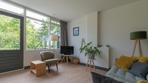 A modern living room with a sofa, a chair, a TV, a plant, and a lamp. - De Zeester 4-person Holiday Home n De Koog (Callantsoog)