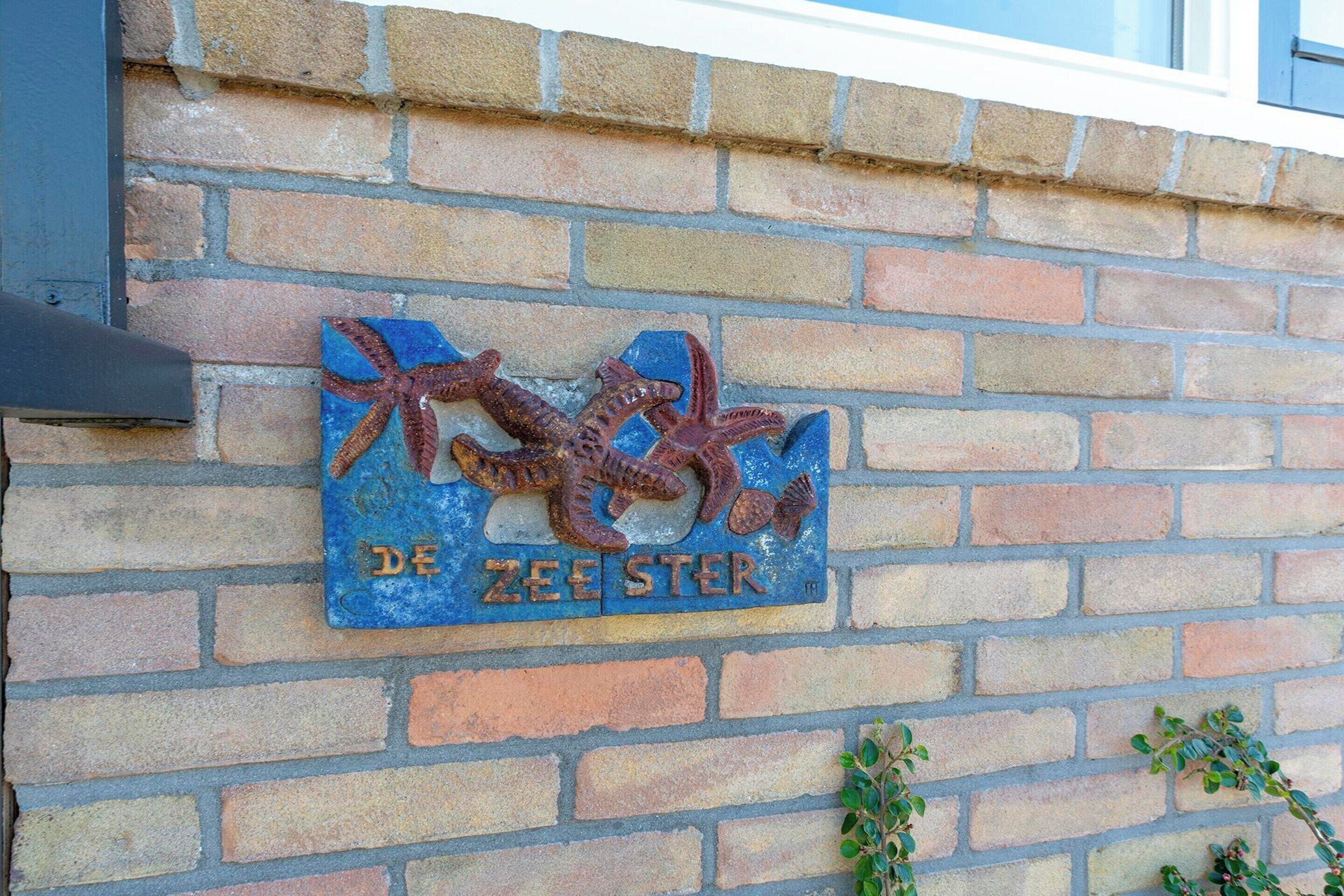 A brick wall with a sign that reads "DE ZEESTER" and features a decorative fish sculpture.