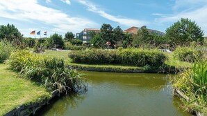 Ein friedlicher Außenbereich mit Teich, üppiger Bepflanzung und einem Gebäude im Hintergrund mit mehreren Flaggen.