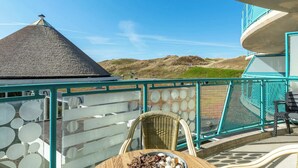 Ein Balkon mit Blick auf Dünen, ein Korbstuhl und ein Tisch mit einer Schale voller Dinge.