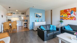 Ein modernes Wohnzimmer mit einer schwarzen Ledersofa, einem Essbereich mit Korbstühlen, einer Küche mit weißen Schränken und einem farbenfrohen abstrakten Gemälde an der Wand.