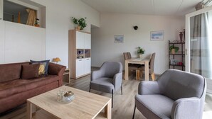 Un salon moderne avec un canapé marron, deux fauteuils gris, une table basse en bois et un coin repas comprenant une table et des chaises.