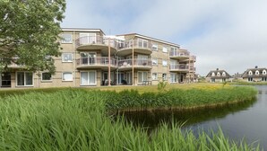 Un edificio residenziale a più piani con balconi, un canale di fronte e una zona verde.