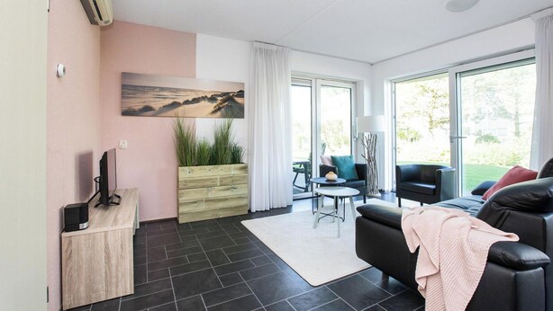 En moderne stue med en sort lædersofa, et træ sidebord med en computer, en glasdør der fører ud til en balkon, og et billede på væggen.