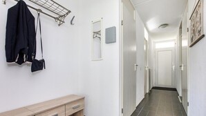 En gang med en træbænk, et knagered med en jakke og en taske, et spejl og en dør i enden.