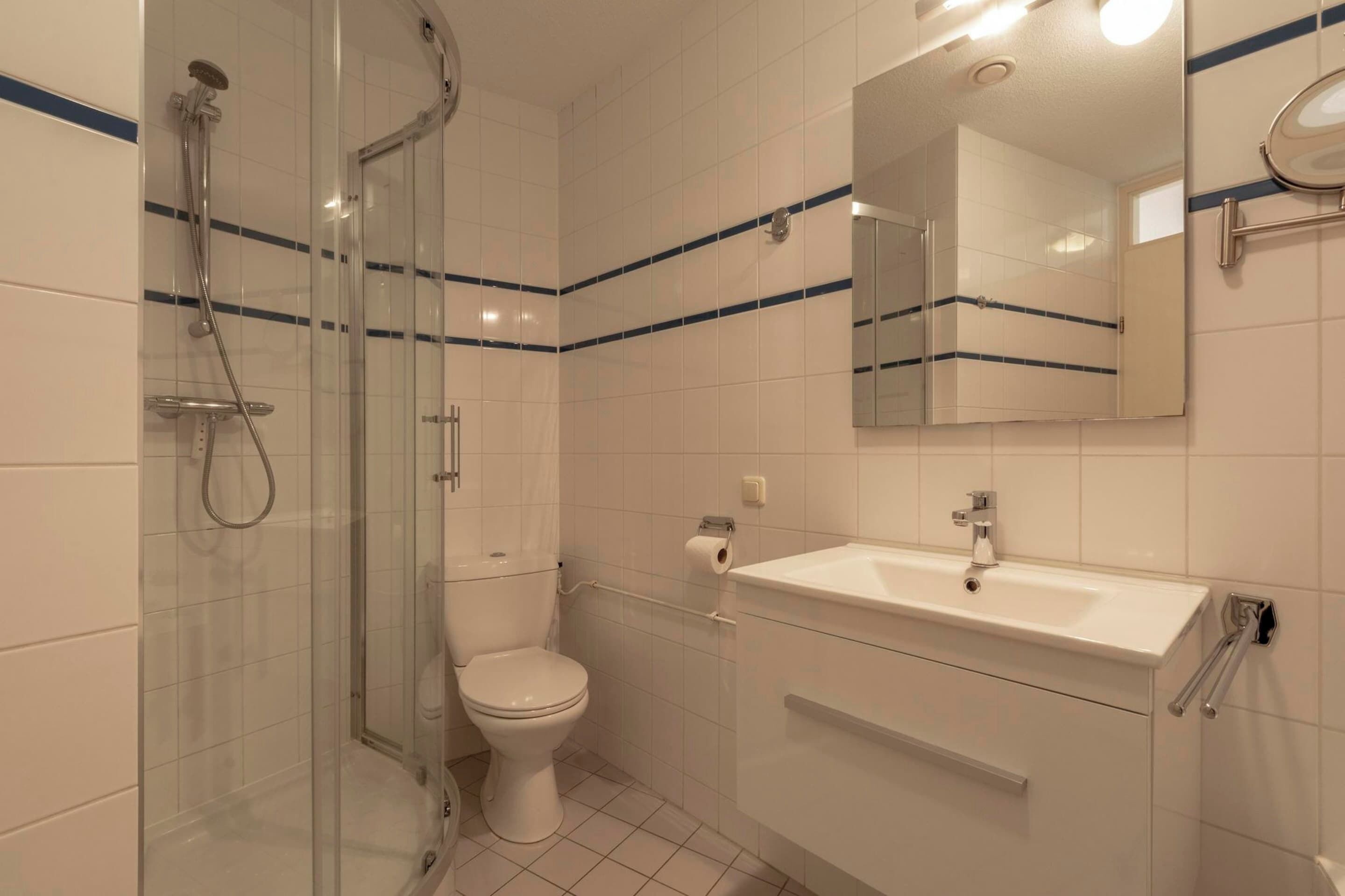A bathroom with a glass-enclosed shower, a toilet, a sink, and a mirror.