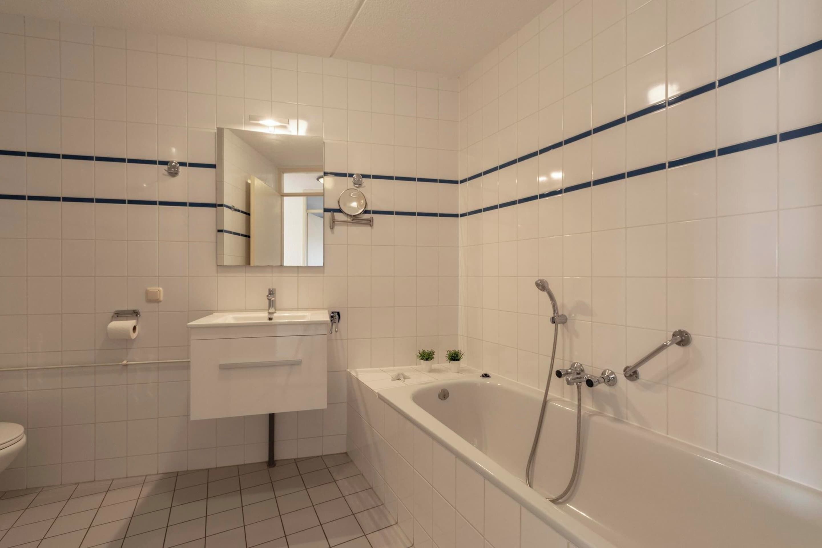 Une salle de bain avec des carreaux blancs, une baignoire, un lavabo, un miroir et des toilettes.