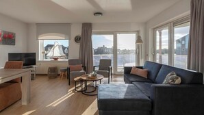 Ein modernes Wohnzimmer mit einer Couch, einem Esstisch und einem Fernseher. Ein großes Fenster bietet Blick auf die Stadt.