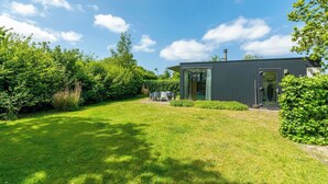A modern house with a well-maintained lawn, a patio with outdoor furniture, and a large window. - Modern Coastal Escape (Sint Maartensvlotbrug)