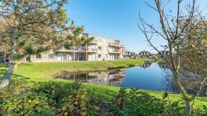 A multi-story residential building with balconies, a small pond in the foreground, and surrounding greenery. - Apartment in Julianadorp Near the Beach (Julianadorp)