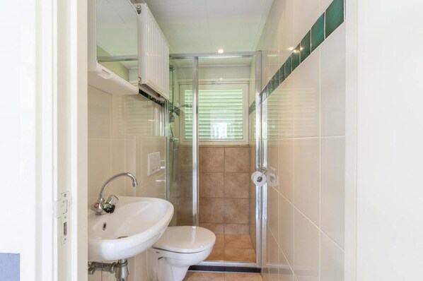 A small bathroom with a glass-enclosed shower, a white sink, and a toilet. - Seaside Getaway With Terrace (Callantsoog)