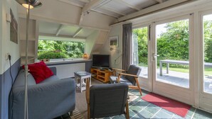 A cozy living room with a sofa, chairs, a TV, and a window overlooking a garden. - Seaside Getaway With Terrace (Callantsoog)