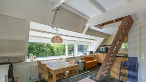 A spacious kitchen with a wooden staircase, a dining area with a table and chairs, and large windows offering a view of greenery outside. - Seaside Getaway With Terrace (Callantsoog)