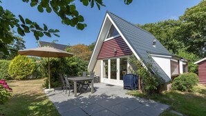 A house with a sloped roof, a patio with a table and chairs, and a covered area with an umbrella. - Seaside Getaway With Terrace (Callantsoog)