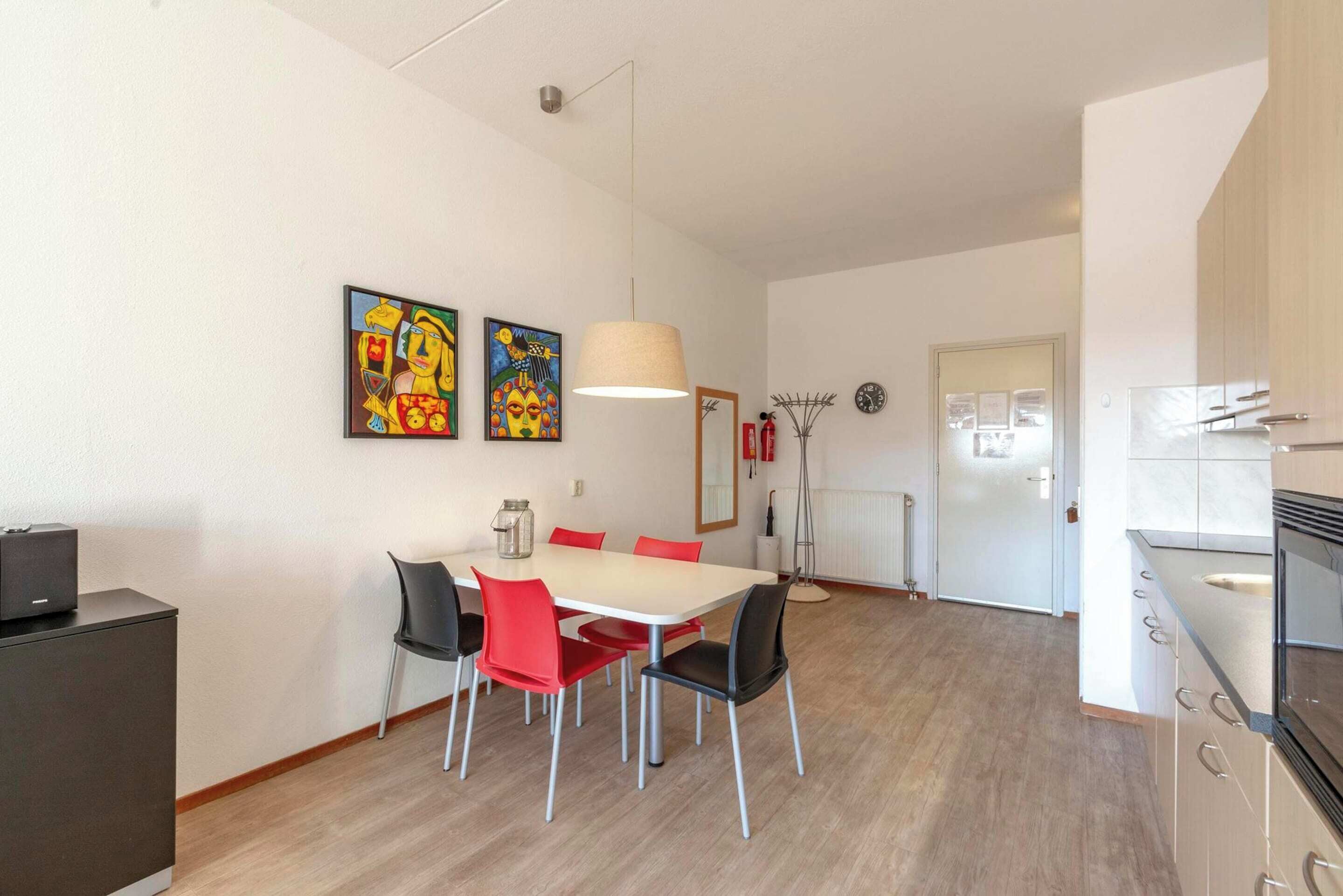 Eine moderne Küche mit weißen Schränken, einem Einbauofen und einer Mikrowelle. Es gibt einen Essbereich mit einem weißen Tisch und roten Stühlen.